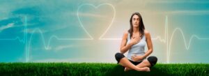 Mulher sentada na grama realizando meditação com um coração ao fundo