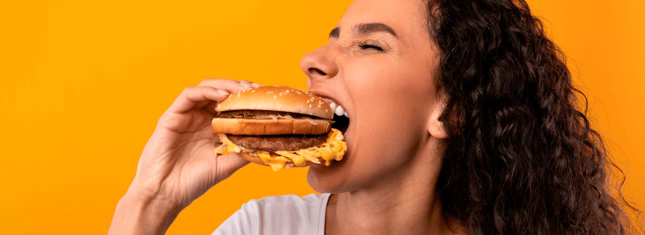 Mulher comendo um hambúrguer, representando como a alimentação pode prejudicar a pele