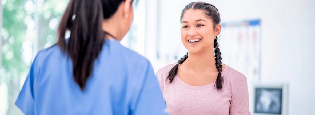 Menina sorrindo conversando com uma médica, retratando sua primeira consulta sozinha