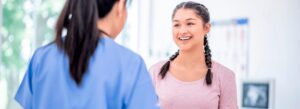 Menina sorrindo conversando com uma médica, retratando sua primeira consulta sozinha