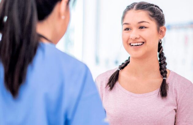 Menina sorrindo conversando com uma médica, retratando sua primeira consulta sozinha