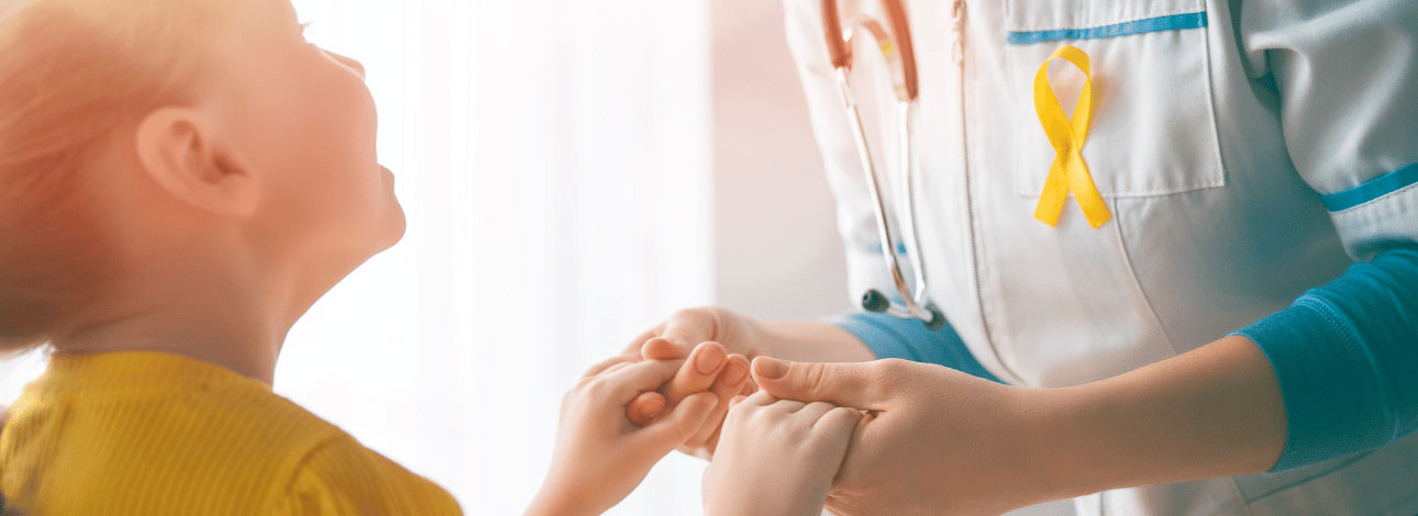 Criança olhando para um médico enquanto segura sua mão, o qual tem uma fita de luta contra o câncer em seu jaleco