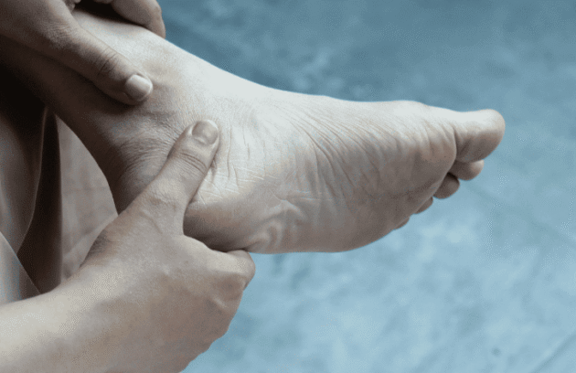 Pessoa com a mão no pé sofrendo com bolhas e calos