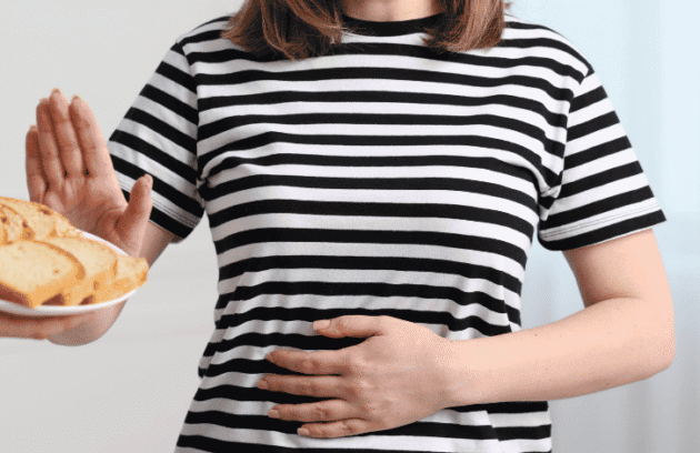 Mulher com a mão na barriga recusando alimento com glúten