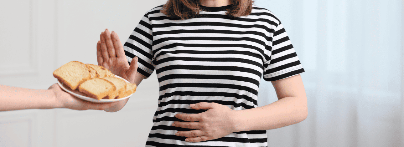 Mulher com a mão na barriga recusando alimento com glúten