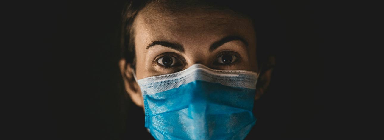 Mulher com máscara cobrindo o rosto em cenário escuro