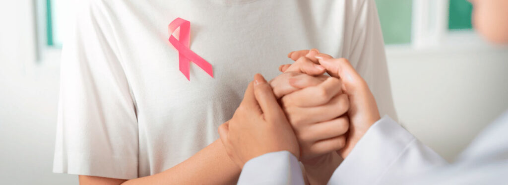 Médico segurando as mãos de paciente com uma fita rosa em menção ao câncer de mama