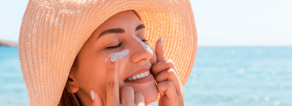 Mulher sorridente de chapéu aplica protetor solar no rosto