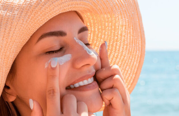 Mulher sorridente de chapéu aplica protetor solar no rosto