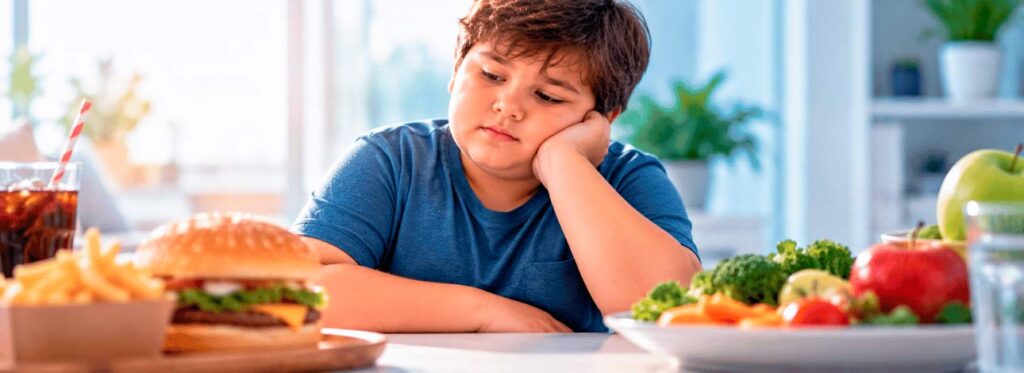 Criança com obesidade sentada à mesa com comida
