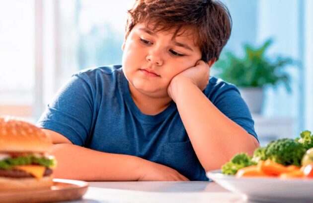 Criança com obesidade sentada à mesa com comida
