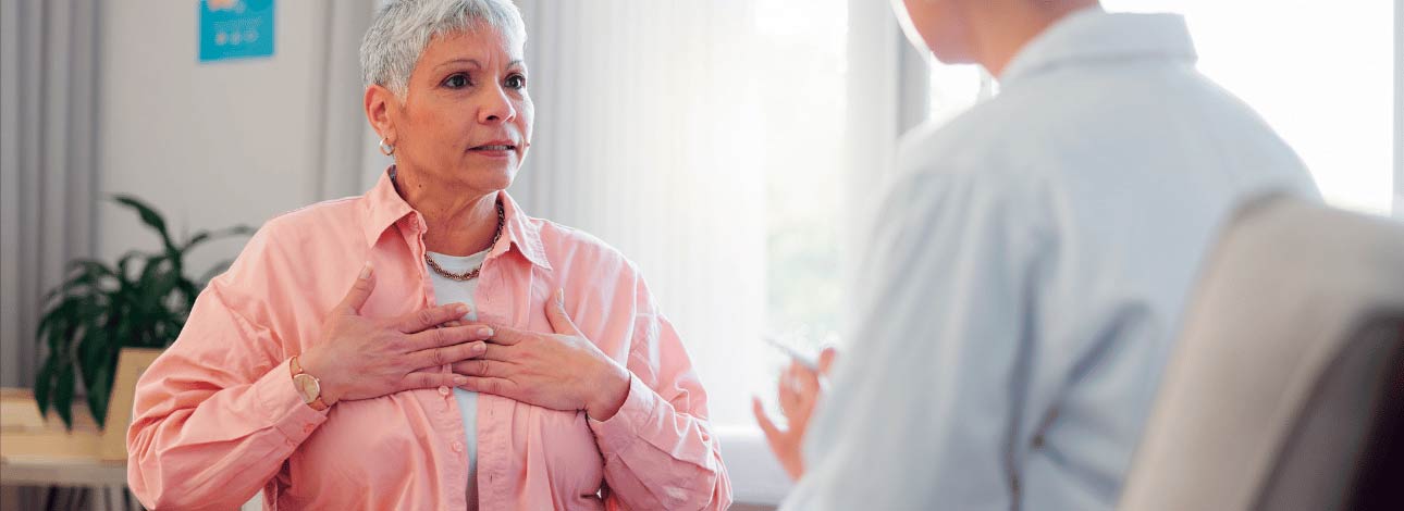 Mulher com a mão no peito em consulta com cardiologista